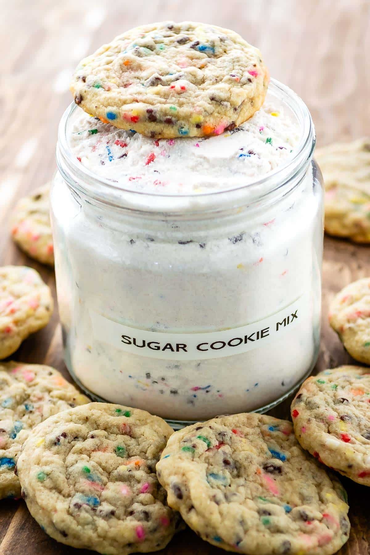 two photos of sugar cookie mix in a big clear container with sugar cookies sitting around the container