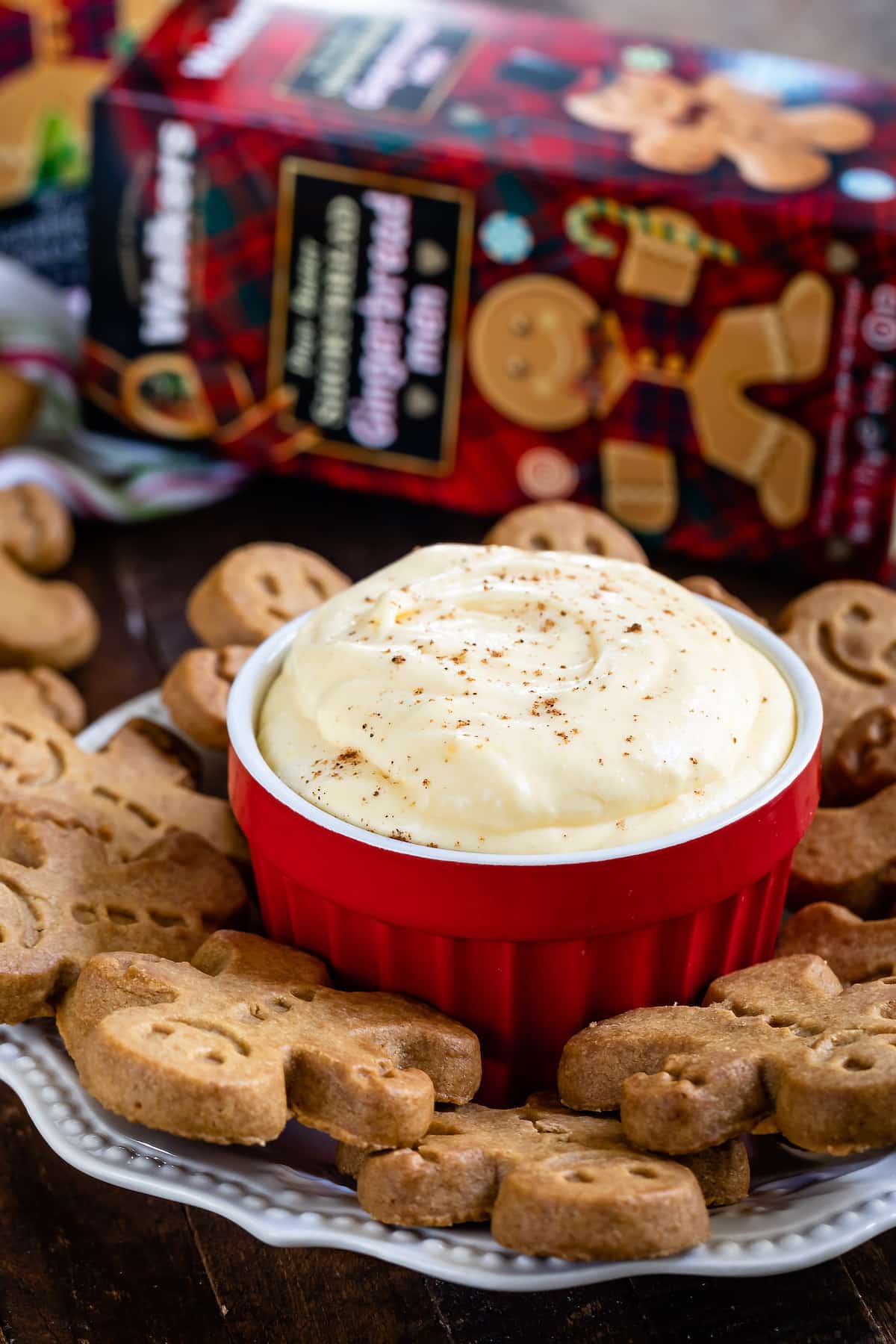 eggnog pudding dip in red bowl on white plate with cookies around