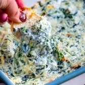 bread being dipped in the spinach dip by a hand