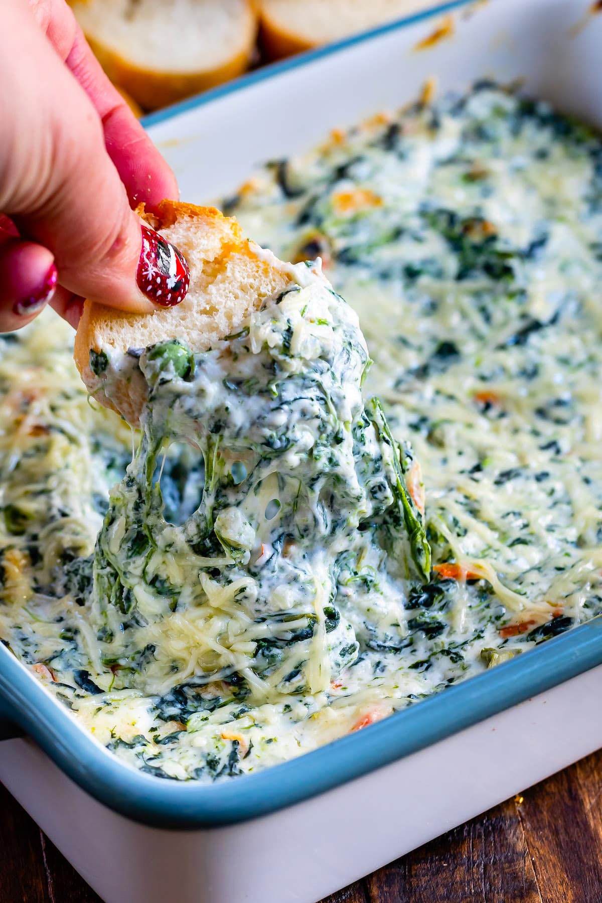 bread being dipped in the spinach dip by a hand