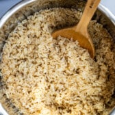 brown rice in a metal bowl with a wooden spoon in the rice