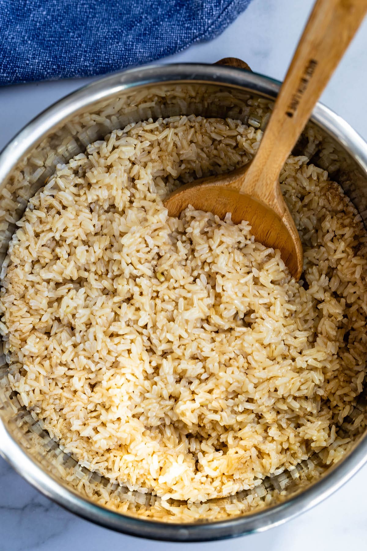 brown rice in a metal bowl with a wooden spoon in the rice