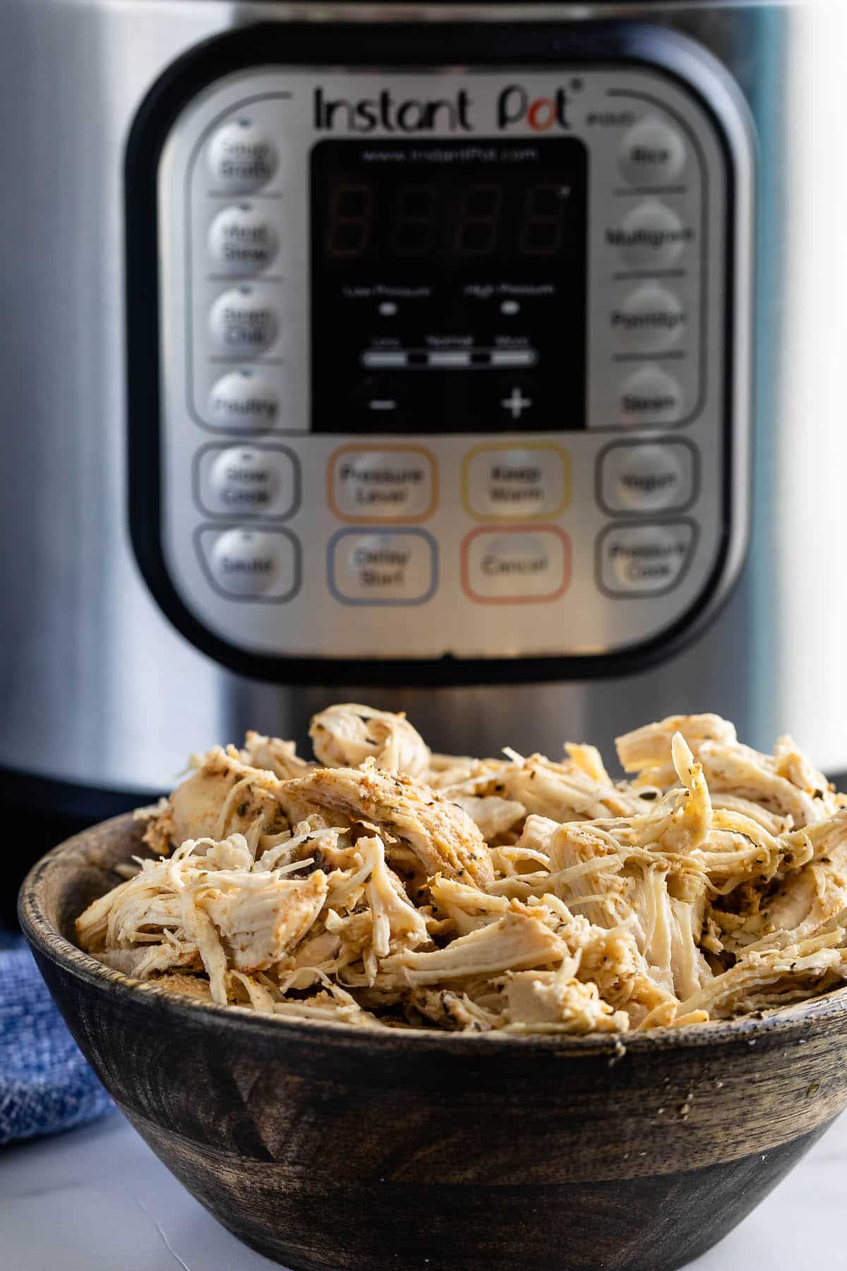 shredded chicken in a brown bowl with an instant pot behind