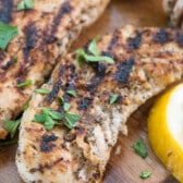 chicken on a cutting board next to lemons and herbs