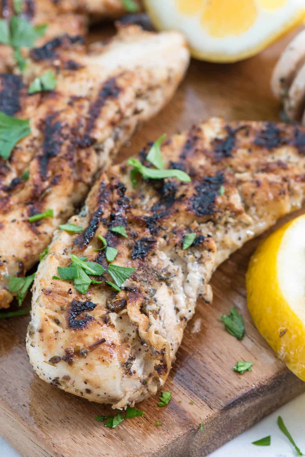 chicken on a cutting board next to lemons and herbs