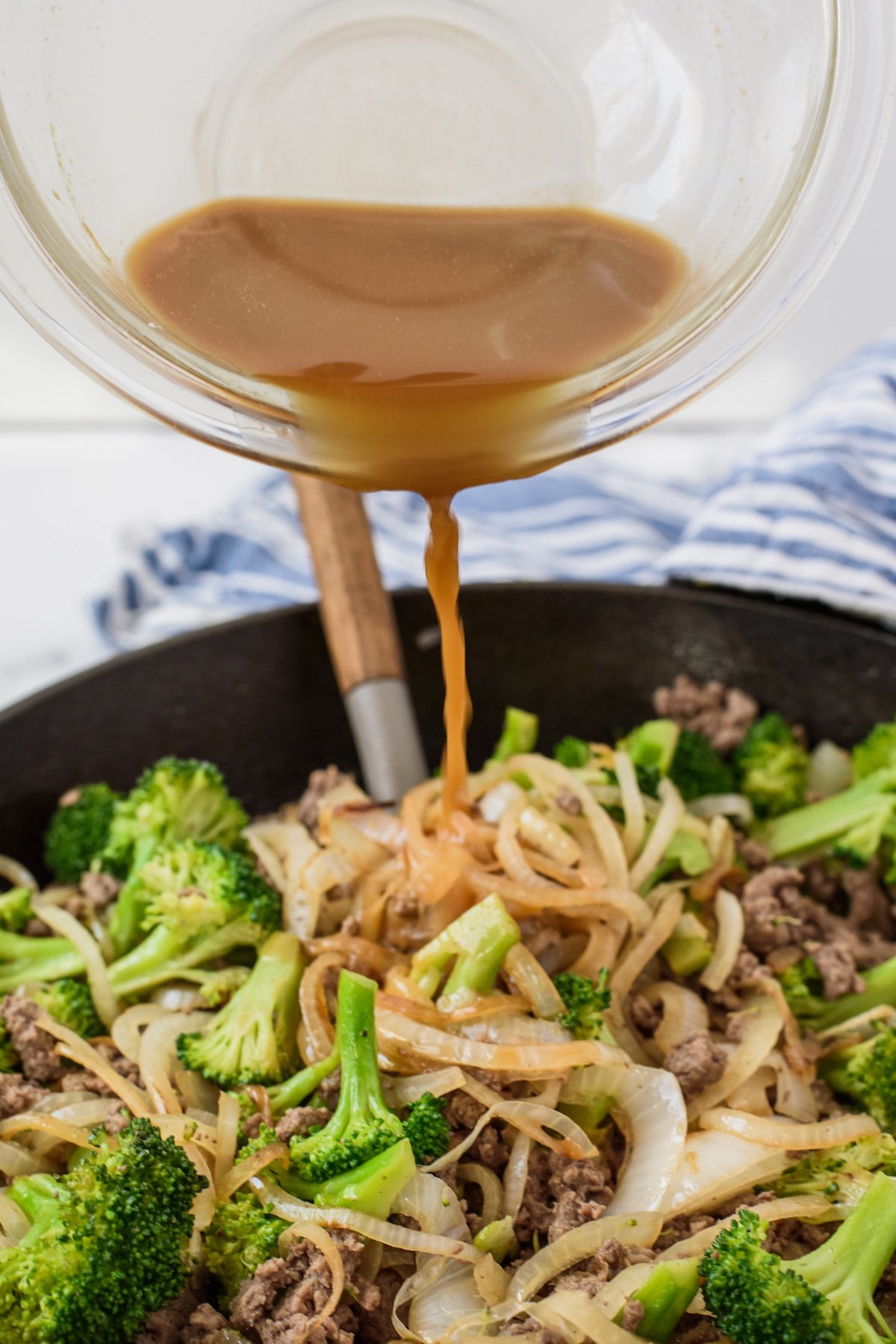 beef, broccoli and other things mixed together in a black pan with sauce being poured in