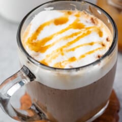 latte in a clear glass with froth and caramel drizzle on top