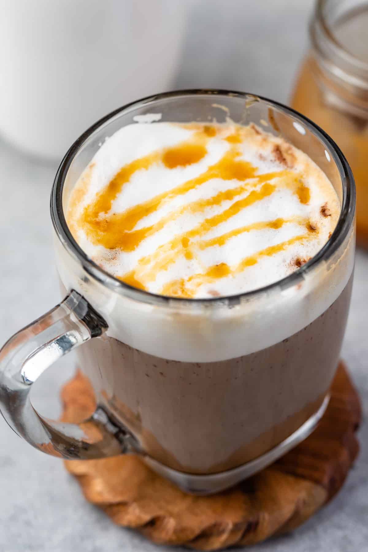 latte in a clear glass with froth and caramel drizzle on top