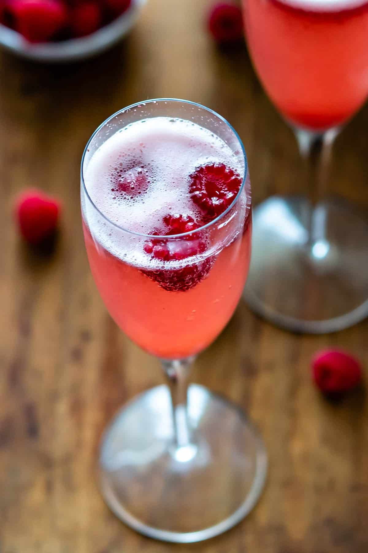 pink drink in a tall glass with raspberries around it
