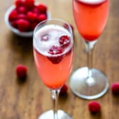 pink drink in a tall glass with raspberries around it