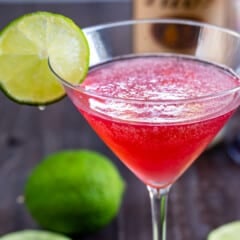 clear cocktail glass with a red drink and lime on the rim