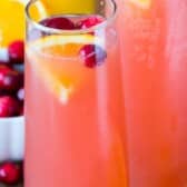 two glasses filled with pink drink with cranberries and orange slices in the glass with words on top