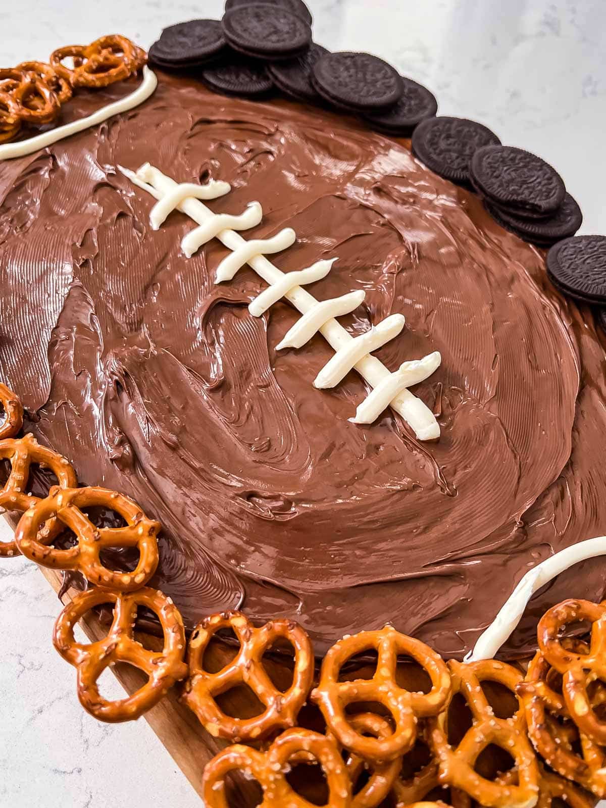nutella shaped as a football with lines drawn in white surrounded by pretzels and Oreos