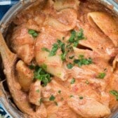 pasta covered in sauce in a metal pan with a wooden spoon with words on top of the image