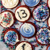 red velvet cookies with white frosting and blue and purple toppings