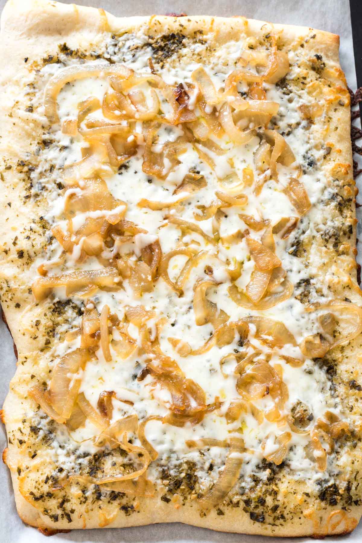 flatbread with onions and pesto on top laid out on a cutting board