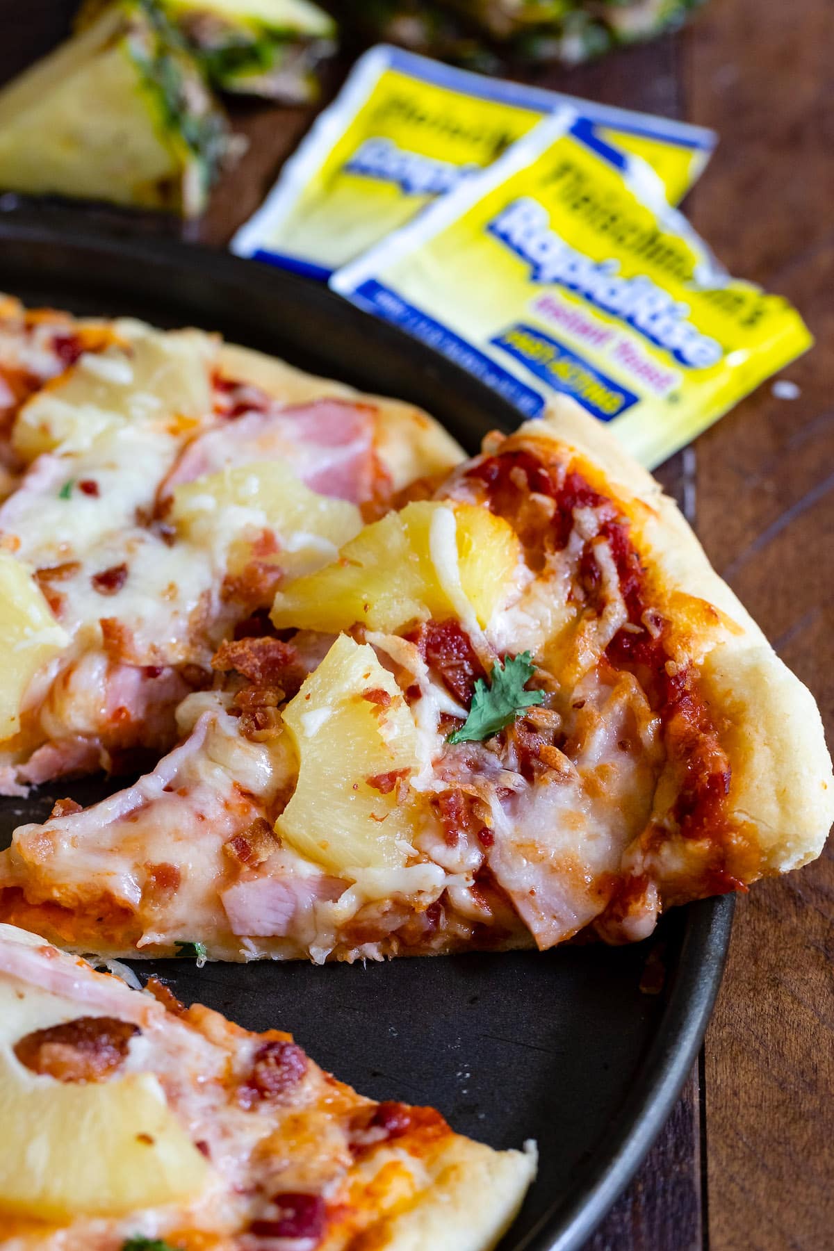 hawaiian pizza with ham and pineapple on top in a black pan