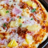 hawaiian pizza with ham and pineapple on top in a black pan