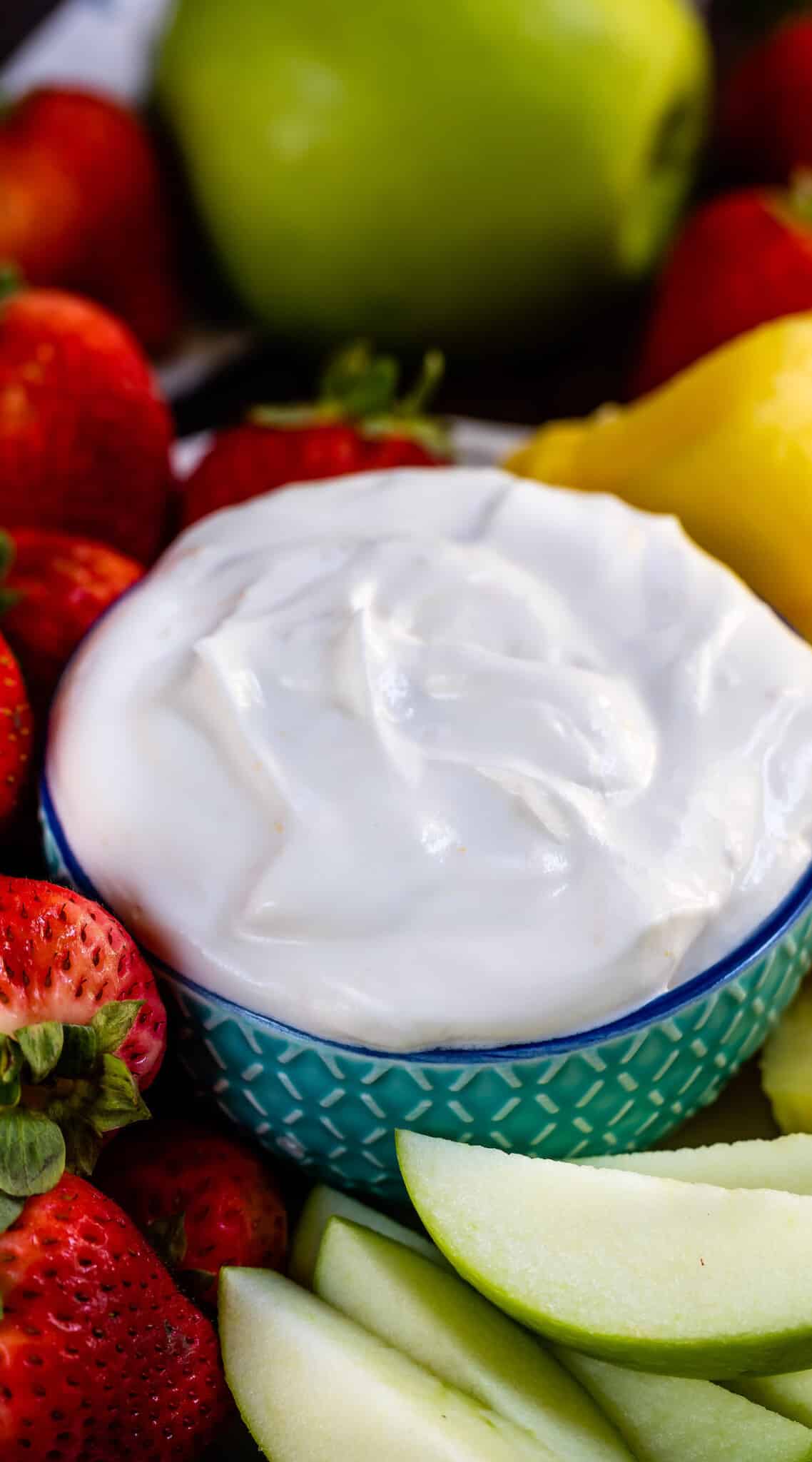 white fluff dip in a teal bowl surrounded by fruit