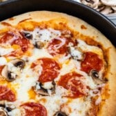 deep dish pizza in a black pan with pepperoni on top with words on top