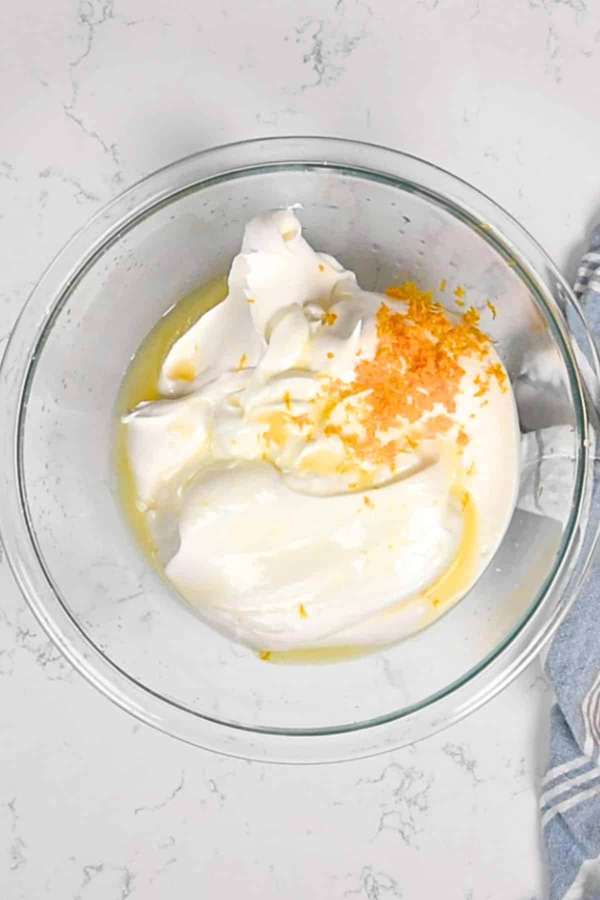 clear bowl of whipped topping yogurt and orange zest on counter.