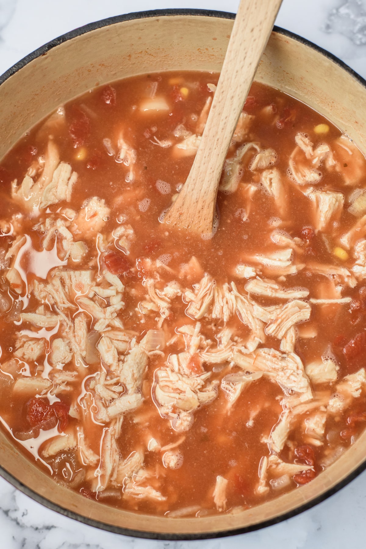 soup in pot with shredded chicken and wooden spoon