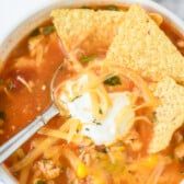 salsa soup in white bowl with sour cream and tortilla chips and cheese with spoon