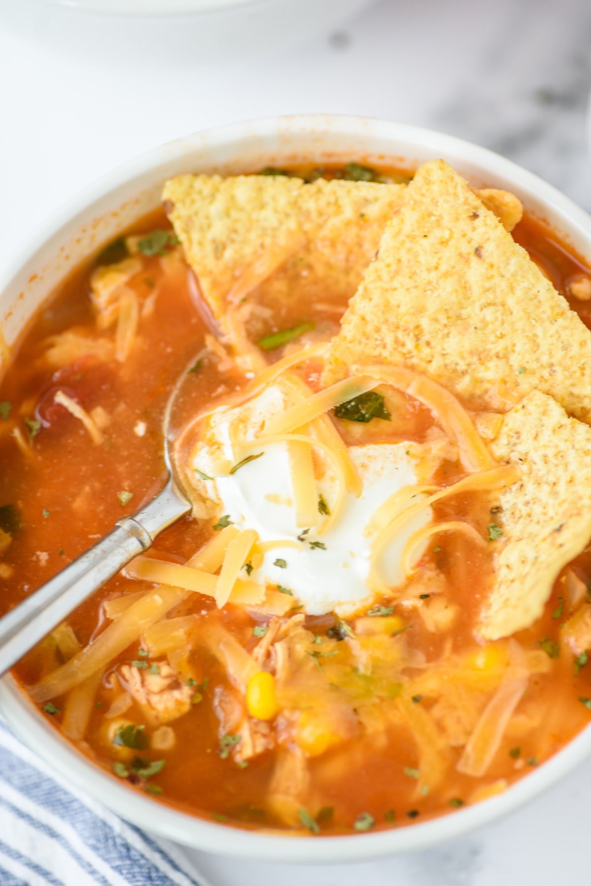 salsa soup in white bowl with sour cream and tortilla chips and cheese with spoon