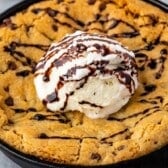 A large chocolate chip cookie baked in a skillet, this classic pizookie recipe is topped with a scoop of vanilla ice cream and drizzled with chocolate syrup.