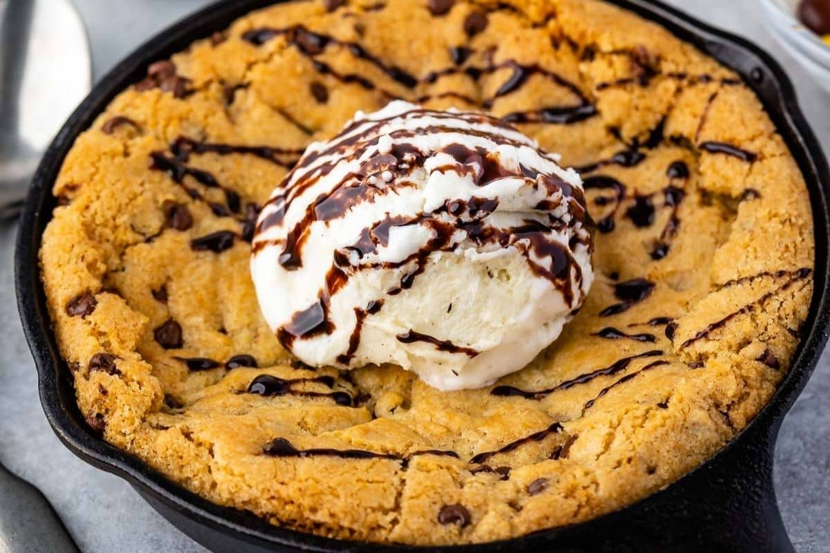 A large chocolate chip cookie baked in a skillet, this classic pizookie recipe is topped with a scoop of vanilla ice cream and drizzled with chocolate syrup.