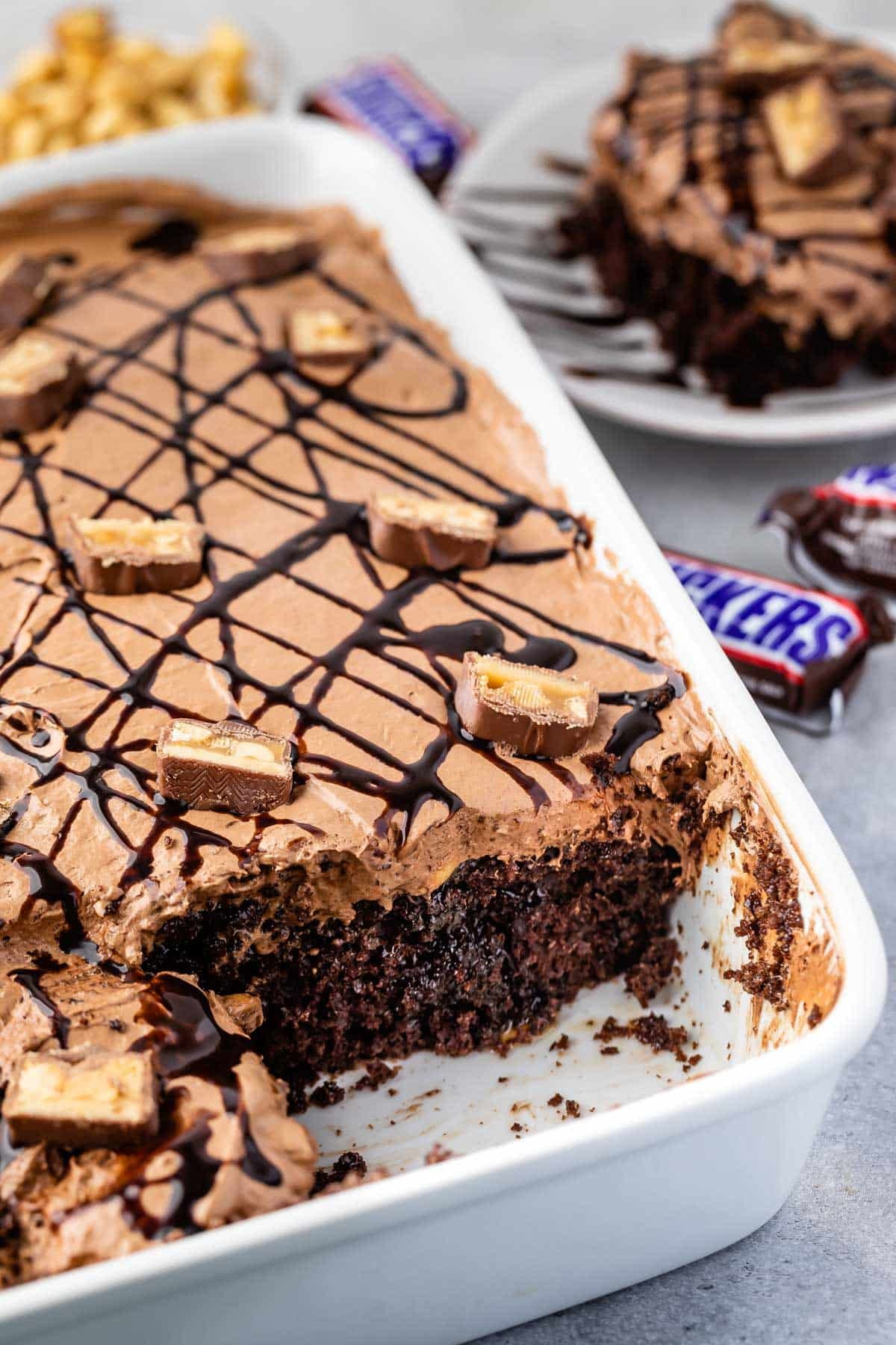 snickers poke cake in a white dish with snickers on top