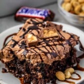 one square slice of snickers poke cake on a white plate