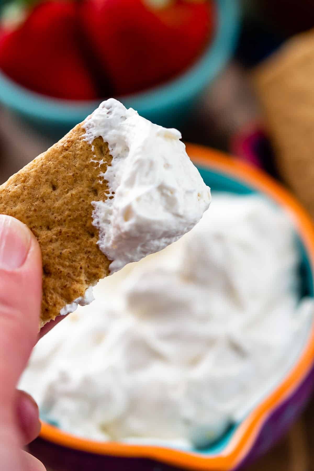 white dip in a purple bowl with a hand dipping a cracker into it