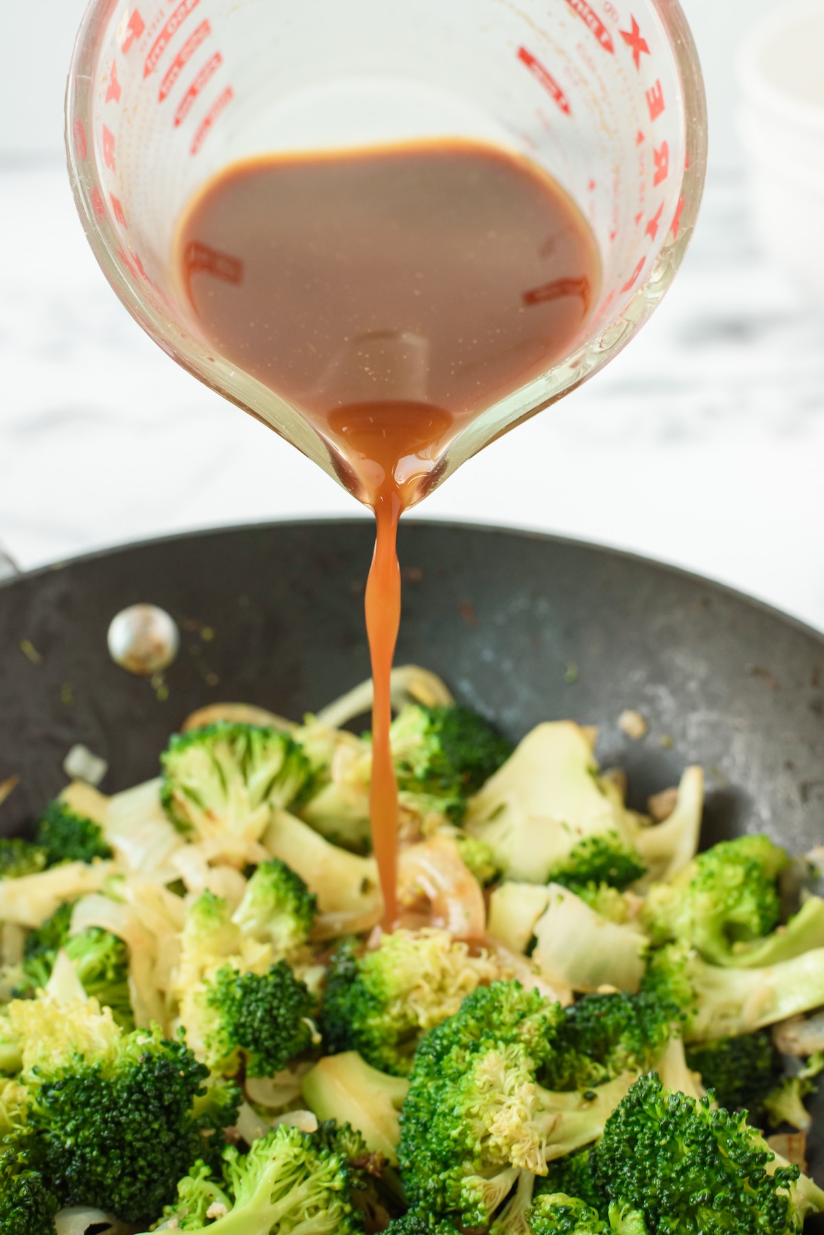 sauce being poured into broccoli and meat mixed together in a black pan