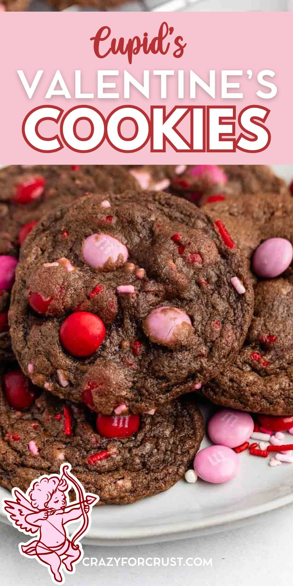A plate of Valentine Cookies with red and pink candy pieces and sprinkles, styled for Valentines Day. The text above reads Cupids Valentines Cookies with a cartoon cupid in the corner.