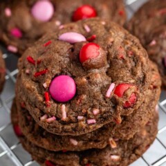 A stack of Valentine Cookies with red, pink, and purple candy-coated chocolates and sprinkles rests on a metal cooling rack.