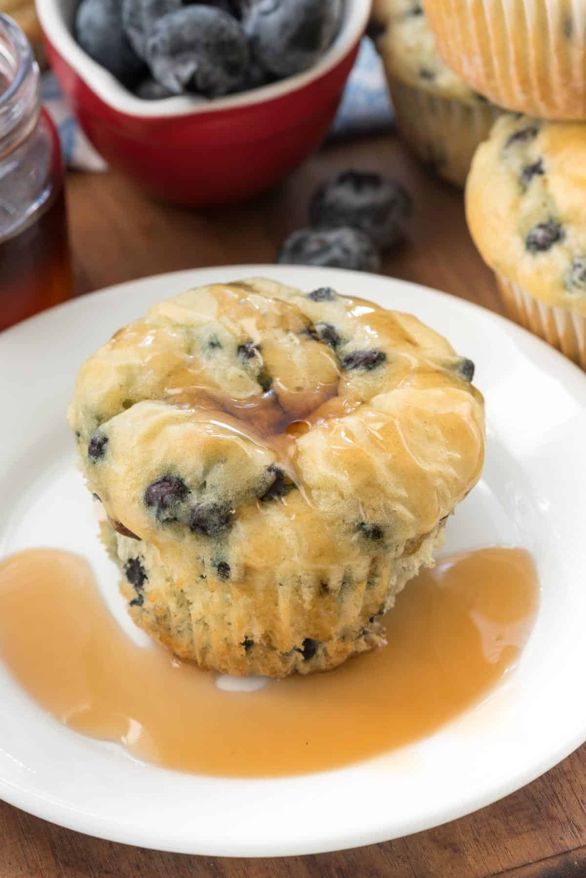 muffin on a white plate with syrup and blueberries baked in.