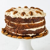 carrot cake layered with white frosting and decorated with pecans.