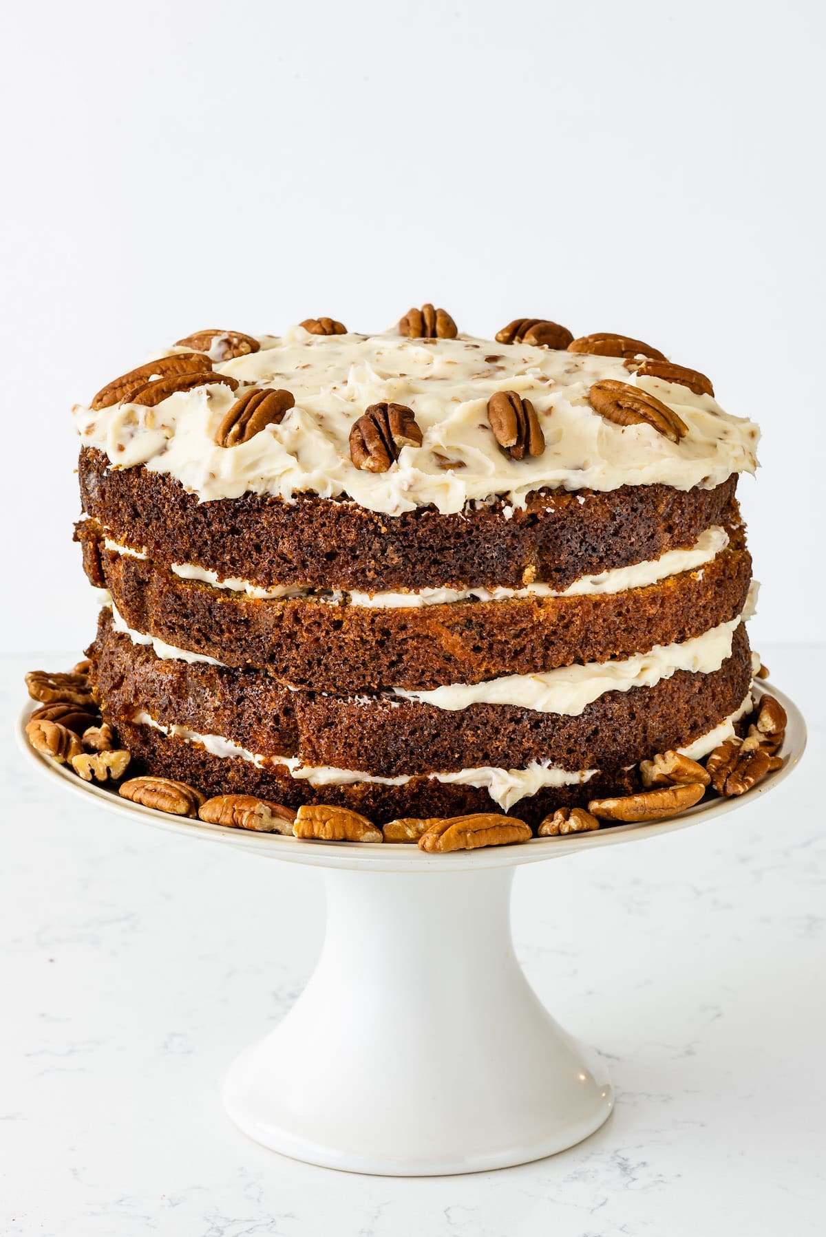 carrot cake layered with white frosting and decorated with pecans.