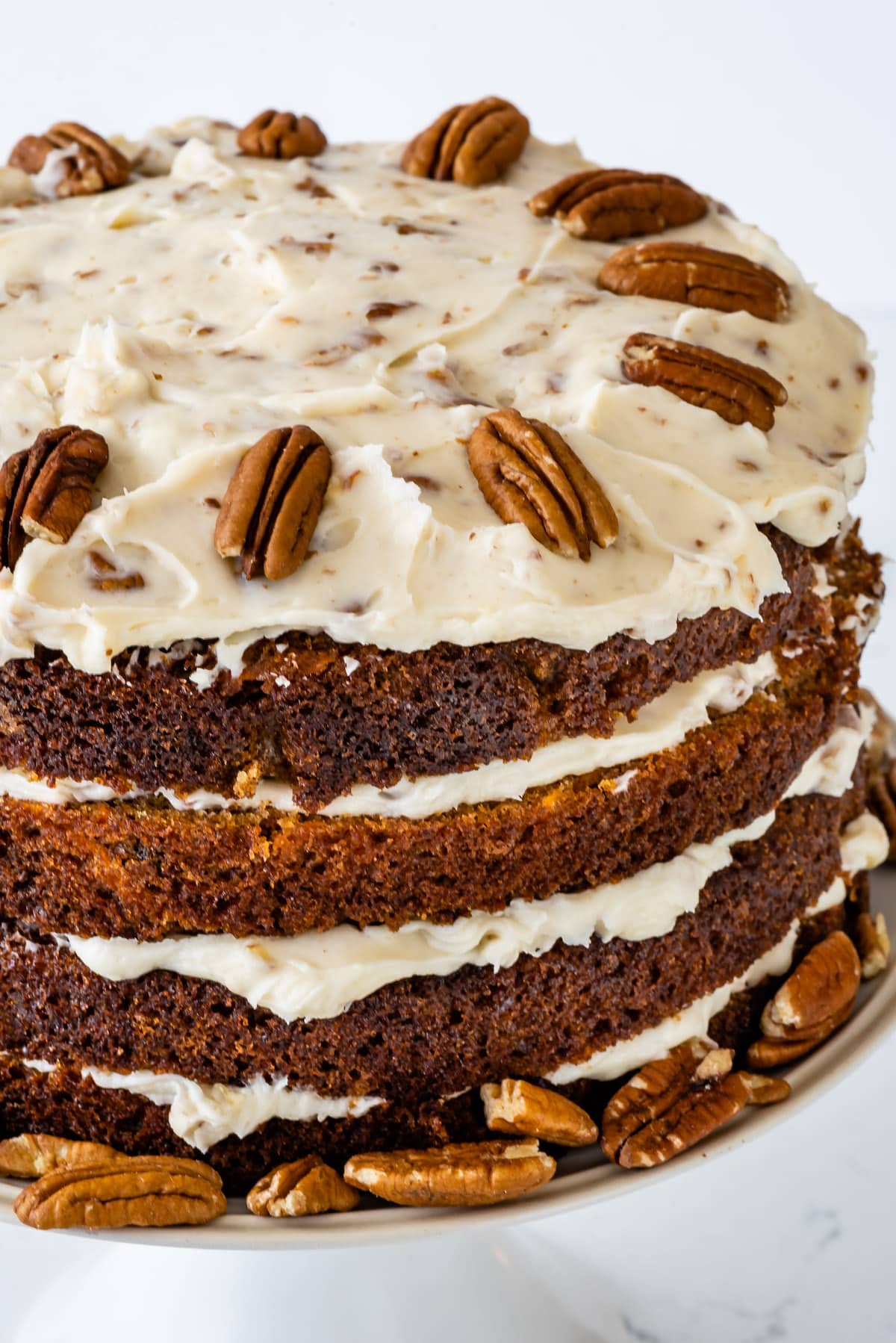 carrot cake layered with white frosting and decorated with pecans.