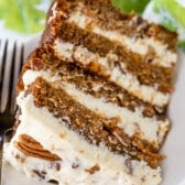 carrot cake layered with white frosting and decorated with pecans on a white plate.