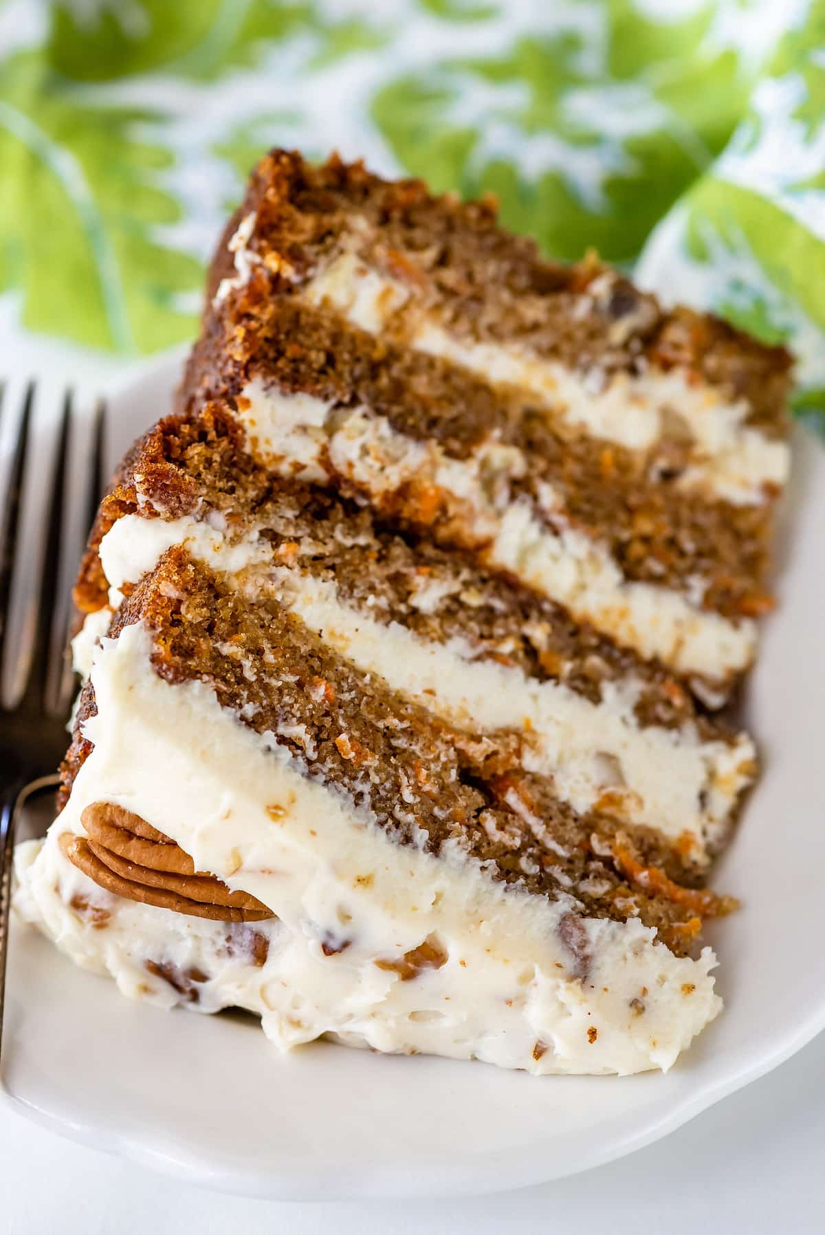 carrot cake layered with white frosting and decorated with pecans on a white plate.