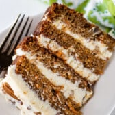 carrot cake layered with white frosting and decorated with pecans on a white plate.