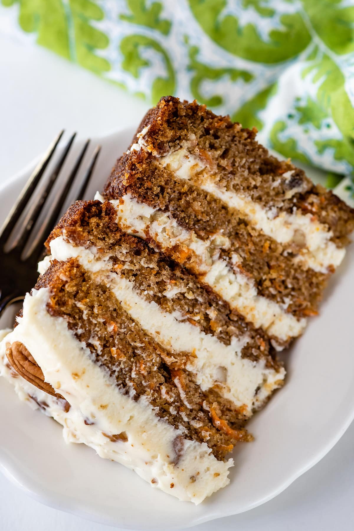 carrot cake layered with white frosting and decorated with pecans on a white plate.