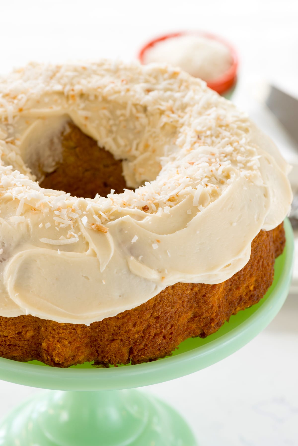 carrot cake on a mint green cake stand covered in white frosting.