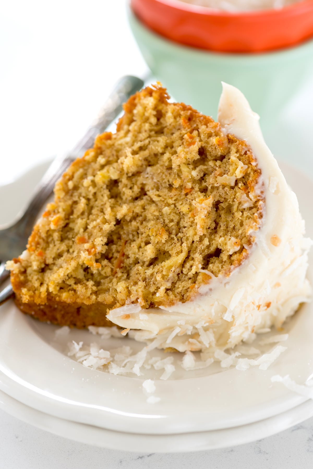 one slice of carrot cake on a white plate covered with white frosting.