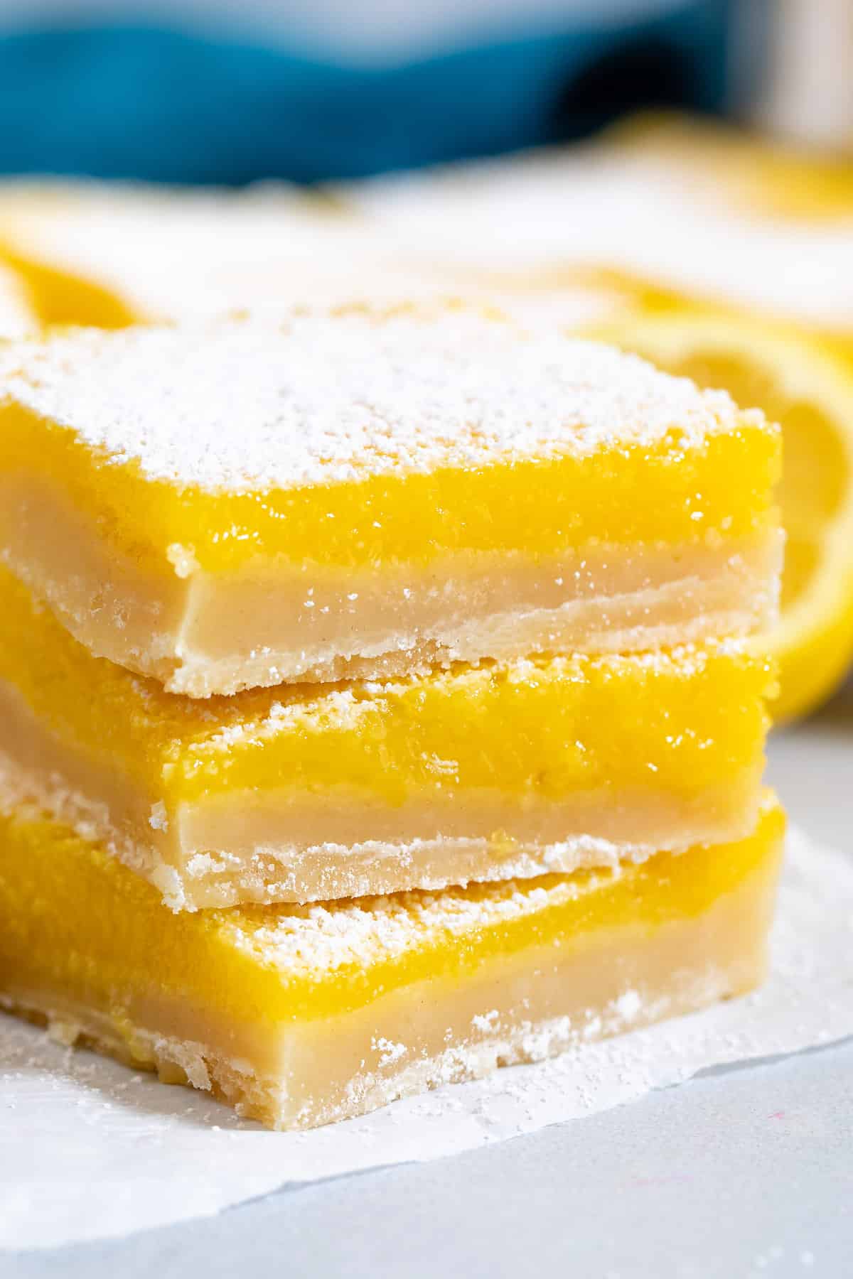 stacked lemon bars with powdered sugar on top around cut lemons.