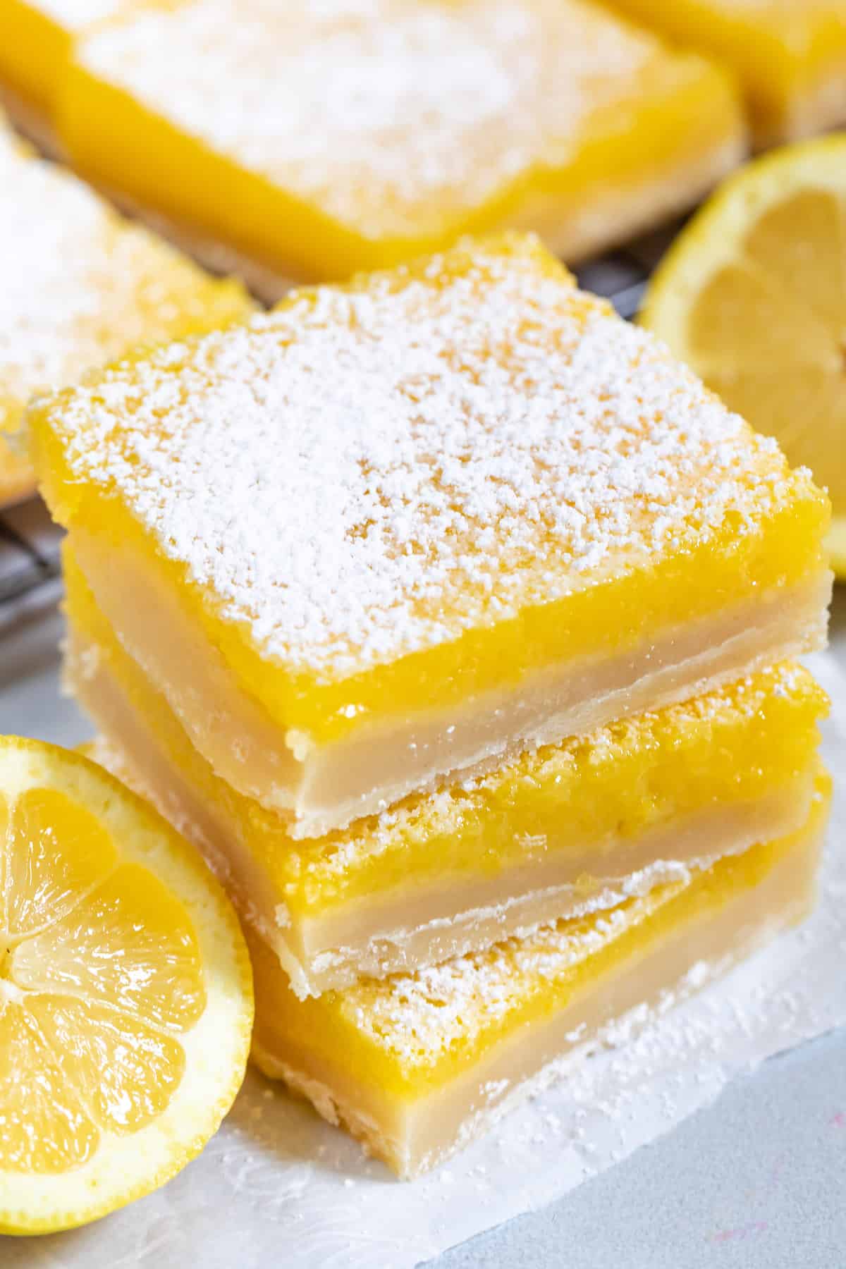 stacked lemon bars with powdered sugar on top around cut lemons.