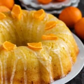 orange bundt cake with sliced oranges and icing on top on a white plate.