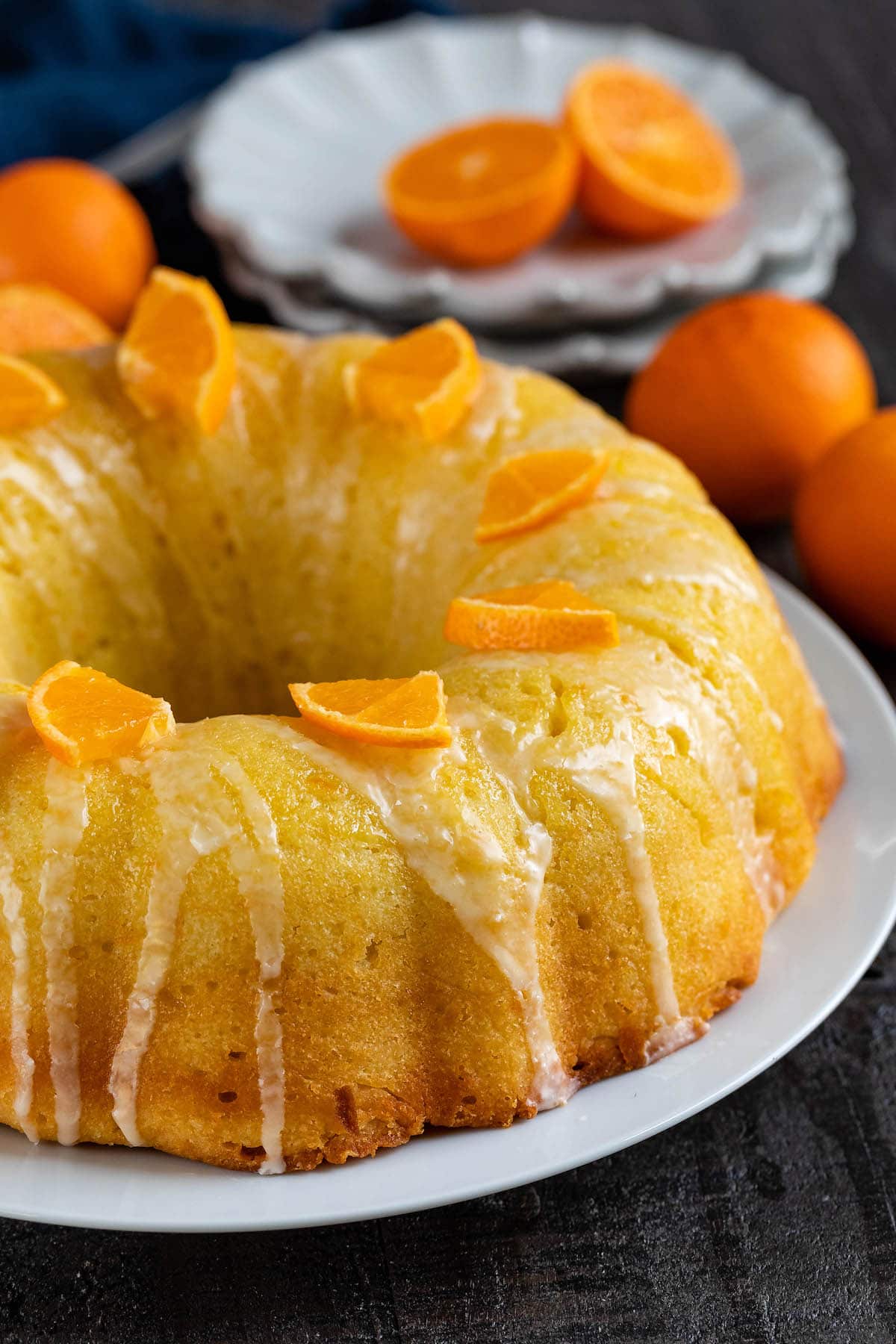 orange bundt cake with sliced oranges and icing on top on a white plate.